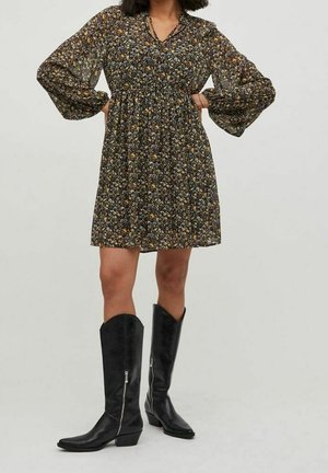 Vestido negro con flores, de mangas largas abullonadas, cintura fruncida y con un dobladillo a la altura de la rodilla. Combinado con botas de cuero negro hasta la rodilla con cremalleras.
