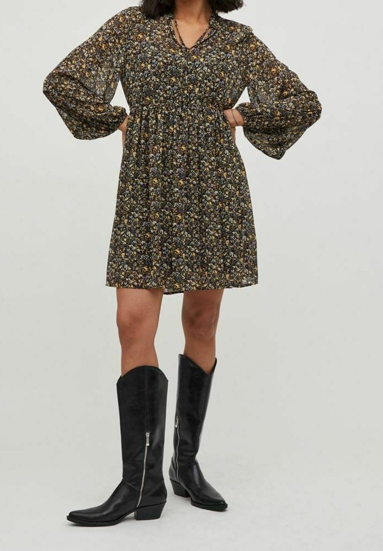 Svart blommig klänning med långa puffärmar, sammanfald midja och knä-lång fåll. Kombinerad med knähöga svarta läderstövlar med blixtlås.