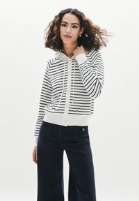 Cardigan con cappuccio a righe in crema e navy, caratterizzato da una chiusura frontale a bottoni, cappuccio e polsini a coste. Tessuto a maglia morbido con una vestibilità comoda.