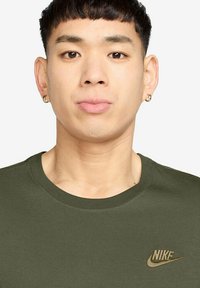 Olijfgroene katoenen T-shirt met een ronde halslijn en korte mouwen; voorzien van een gouden Nike-logo geborduurd op de borst.