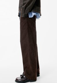 Ruske leve jeans hlače s teksturiranim finišem, ki vsebujejo stranske žepke in so v paru z sijočimi črnimi loafers.