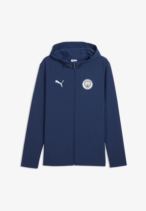 Marineblaue Kapuzenjacke mit durchgehendem Reißverschluss und subtilem Muster, Puma-Logo auf der rechten Brust und Manchester City Emblem auf der linken Brust.