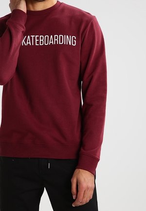 Maroon sweatshirt with a crew neckline, featuring the word "SKATEBOARDING" in bold white text across the front. Soft fabric with ribbed cuffs.