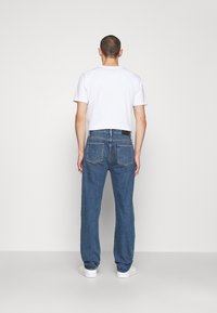 Hombre visto de espaldas vistiendo una camiseta de algodón blanca y jeans de mezclilla azul. Los jeans tienen un diseño de pierna recta y dos bolsillos traseros.