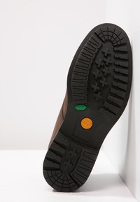 Brown leather boot with a black rubber sole featuring various tread patterns and colored logos in green and orange on the outsole.