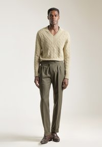 Suéter de punto beige con escote en V, combinado con pantalones de pinzas verdes oliva y zapatos de cuero marrón. Diseño simple, texturizado y a medida.