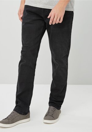 Schwarze Jeans aus Denim mit geradem Schnitt, ausgestattet mit einem klassischen Fünf-Taschen-Design. Kombiniert mit grauen Wildledersneakern, die einen lässigen Look erzeugen.