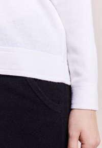 Bílý pletený svetr s texturovaným povrchem, s žebrovaným lemem, v kombinaci s černými pletenými kalhotami s detailem boční kapsy.