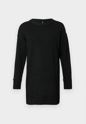 Dlhý čierny pletený sveter s rebrovanými manžetami a lemom, okrúhlym výstrihom a spustenými ramenami na svetlošedom pozadí.