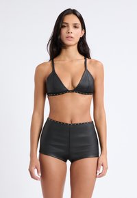 Set bikini nero con reggiseno triangolare adornato da borchie metalliche, abbinato a pantaloni corti a vita alta, il tutto in una finitura liscia e testurizzata.