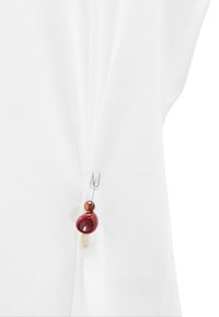 Biała odzież o drapowanej konstrukcji z metalowym agrafką w kolorze srebrnym i trzema ozdobnymi koralikami: czerwonym, bursztynowym i kremowym. Gładka tekstura.