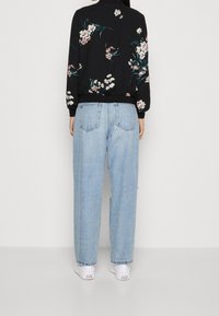 Czarny sweter z kwiatowym wzorem i długimi rękawami, w zestawieniu z jasnoniebieskimi, luźnymi dżinsami. Białe sneakersy widoczne na dole.