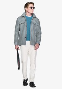 Tjekket jakke i hvid, sort og blå, lagdelt over en teal strikket sweater, parret med hvide bukser og sorte sko, mens der holdes en tennisracket.