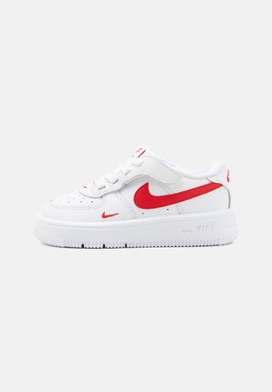 Baltie Nike kedas ar sarkaniem akcentiem un logotipu, ar auklām saistāms dizains, gluda ādas materiāls un teksturēta gumijas zole.
