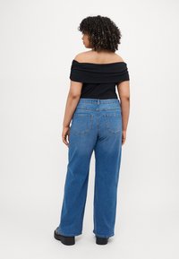 Μαύρη μπλούζα με γυμνά ώματα και μπλε τζιν σε φαρδιά γραμμή, κατασκευασμένη από τζιν, με δύο πίσω τσέπες και ψηλή μέση. Μαύρες πλατφόρμες.