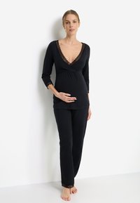 Czarny zestaw odzieży ciążowej do wypoczynku, składający się z kopertowej bluzki z koronkową lamówką i rękawami 3/4 oraz spodni z elastycznym pasem i koronkowymi detalami.