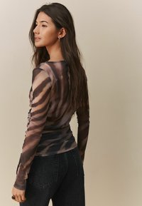 T-shirt à manches longues en tissu transparent et extensible avec un imprimé animal brun et noir. Présente une silhouette ajustée et un col rond.