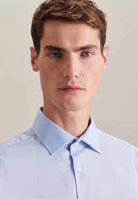 Light blue button-up shirt made of smooth fabric, featuring a spread collar and a plain design with no patterns or accents.