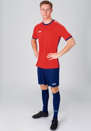 Rotes sportliches Trikot mit blauen Akzenten, kombiniert mit navyfarbenen Shorts und Socken. Enthält ein Logo auf der Brust und den Socken. Strukturiertes Gewebe, figurbetonter Schnitt.