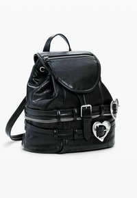 Mustast nahast seljakott, millel on ümar kaanega kaas, hõbedane lukk ja südamekujuline detail, reguleeritavad rihmad ja pannaldega kaunistused.