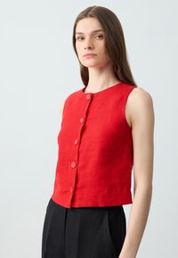 Top senza maniche in lino rosso con scollatura tonda, chiusura frontale a bottoni e una piccola tasca. Tessuto testurizzato con un design accorciato.