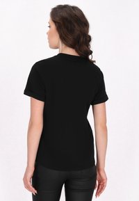 Tricou negru cu mânecă scurtă, fabricat dintr-un material moale, cu manșete răsucite și o croială lejeră, având un gât rotund și fără modele vizibile.