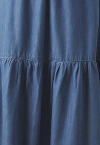 Robe en denim avec un design froncé et un ourlet évasé. Le tissu est d'un bleu foncé uni avec une apparence douce et texturée.