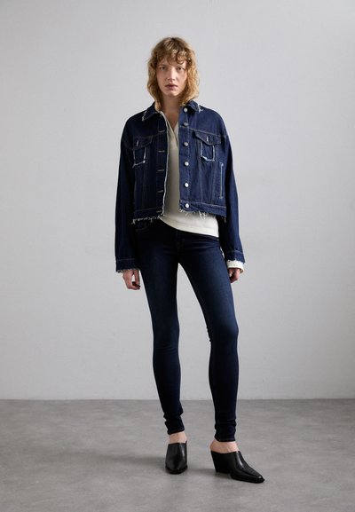 Jeansjack met een rafelige zoom en zakken, gedragen over een lichtkleurig topje. Gecombineerd met donker slim-fit jeans en zwarte hoge muiltjes.