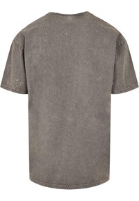 Camiseta de algodón gris con corte relajado, cuello redondo, mangas cortas y una superficie texturada sutil con ligeros desgastes e irregularidades.