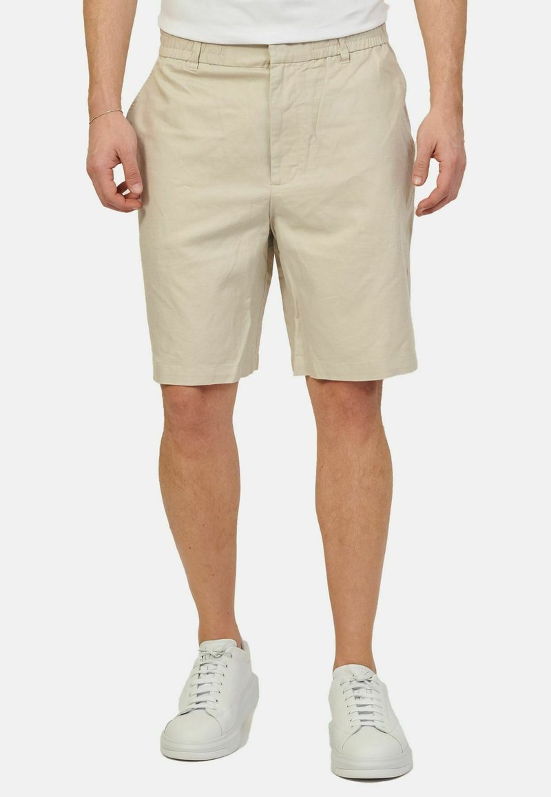 Bermuda in cotone beige con vita elastica, tasche laterali e vestibilità comoda. Abbinati a sneakers bianche per un look casual.