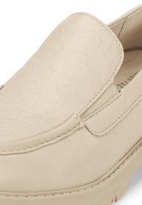 Beige leather slip-on shoe with a rounded toe, textured surface, elastic side panel, and reinforced stitching along the edges.