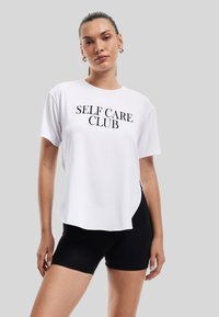 Camiseta blanca con "CLUB DE CUIDADO PERSONAL" impreso en letras negras en negrita, combinada con pantalones cortos negros. Tejido suave, corte relajado, escote redondo.