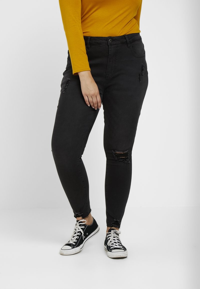 Jeans pitillo negros con detalles desgastados, con roturas en las rodillas y un dobladillo deshilachado. Combinados con zapatillas negras y blancas.