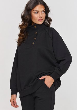 Czarny sweter z wysokim kołnierzem, z czterema guzikami z przodu, ściągaczami na mankietach oraz luźnym krojem. Wykonany z miękkiego materiału.