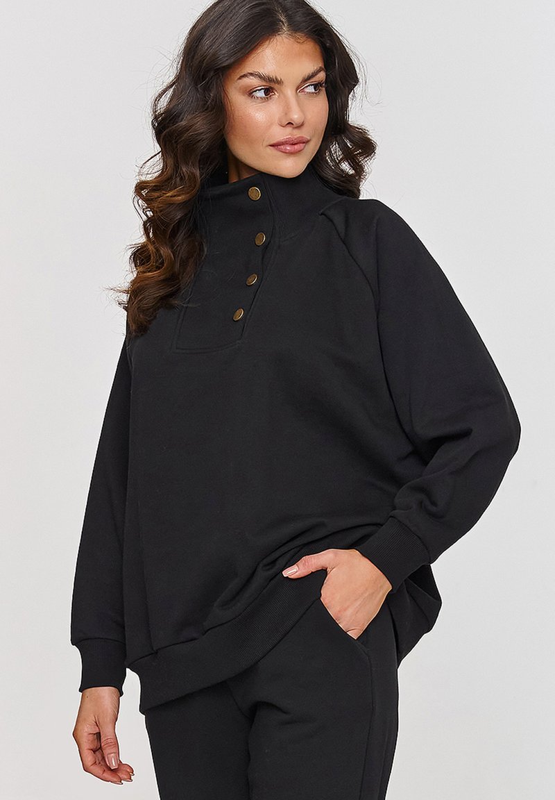 Czarny sweter z wysokim kołnierzem, z czterema guzikami z przodu, ściągaczami na mankietach oraz luźnym krojem. Wykonany z miękkiego materiału.