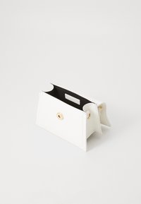 Portefeuille en cuir blanc avec fermeture à poussoir dorée, ouvert sur un intérieur noir. Il présente un design minimaliste avec des lignes épurées et aucun motif visible.