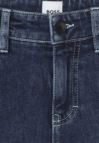 Jeans in denim blu scuro con chiusura a bottone nera, passanti per cintura e etichetta in tessuto bianco con la scritta "BOSS". Dettagli di cucitura visibili.