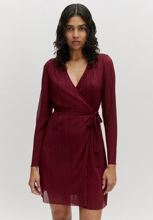 Burgundy wrap dress with long sleeves, v-neckline, and vertical pleats. Ties at the waist with a matching fabric belt. Soft, textured material.