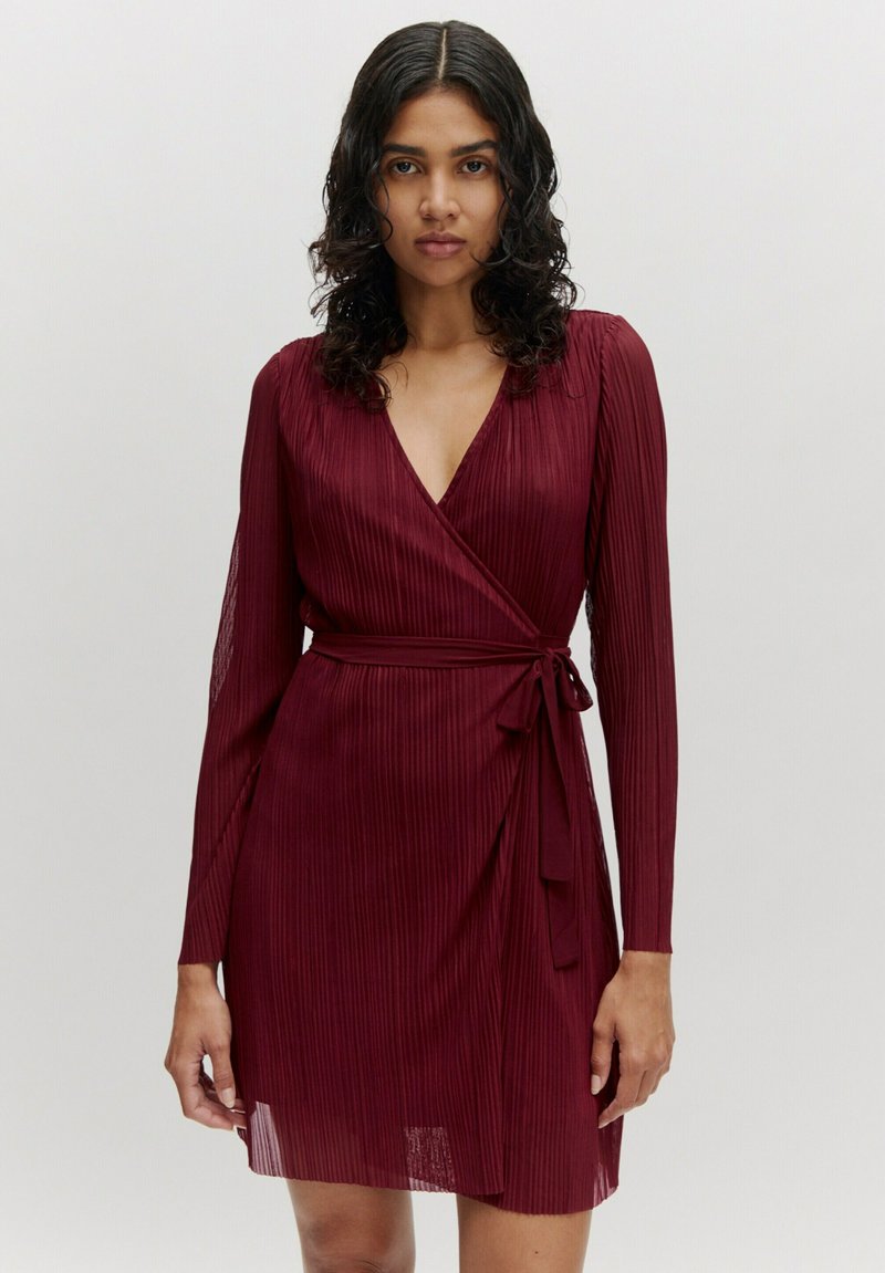 Bordeaux wikkeldress met lange mouwen, v-hals en verticale plooien. Gemaakt om de taille met een bijpassende stoffen riem. Zachte, gestructureerde stof.