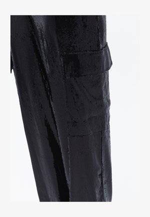 Schwarzer, paillettentexturierter Stoff, maßgeschneidertes Design mit flachen Kanten, verfügt über eine Tasche auf der linken Seite, die das Licht reflektiert und einen glänzenden Effekt erzeugt.