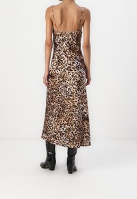 Robe midi en satin à imprimé léopard avec bretelles spaghetti, présentant une texture lisse et une silhouette fluide, assortie à des bottines noires.