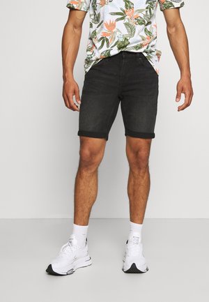 Czarne szorty z denimu z podwiniętymi nogawkami, zestawione z kolorową koszulą w kwiaty i białymi butami sportowymi. Prosty fason, codzienny wygląd.