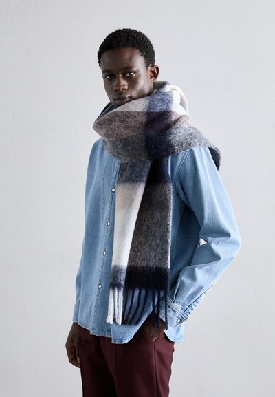 Wool scarf with a plaid pattern in shades of grey, black, and white, draped around the neck, paired with a blue denim shirt.