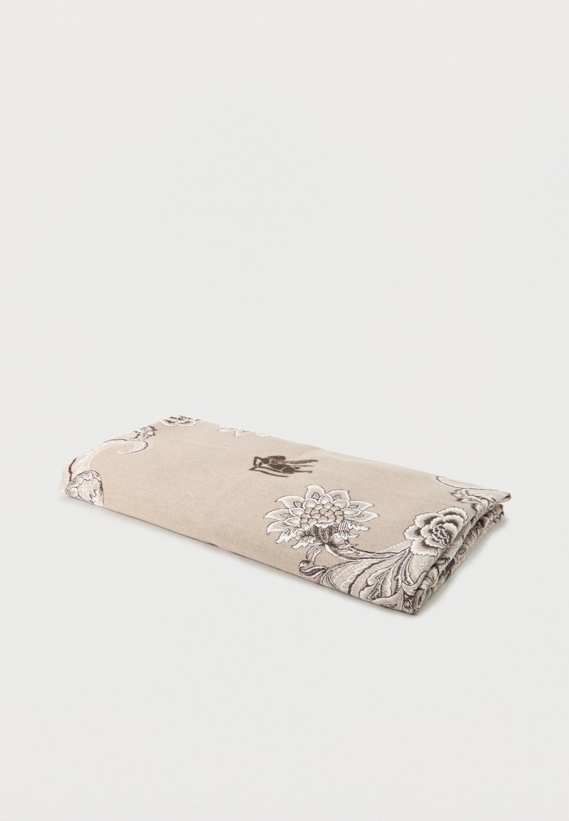 Couverture beige pliée avec des motifs floraux et cachemire blancs et brun foncé sur un fond blanc uni.