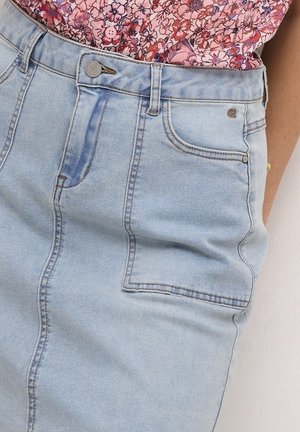 Lichtblauwe denim rok met voor- en zijzakken, metalen knoop en rits, gecombineerd met een roze bloemetjespatroon overhemd dat is ingestopt.