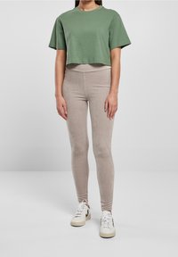 Zkrácený zelený bavlněný tričko spárované s béžovými žebrovanými legínami a bílými teniskami. Legíny mají hladkou texturu a vysoký pas.