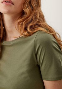Olivengrøn kortærmet t-shirt lavet af glat stof, med rund halsudskæring og diskrete søm langs ærmerne og kanten.