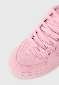 Pink suede sneaker with a smooth texture, round toe, and perforated details. Features matching laces and a low-profile rubber sole.