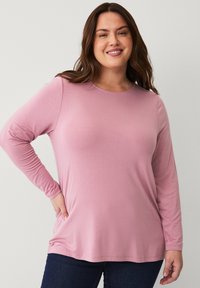 Long-sleeve pink top made of soft fabric, featuring a round neckline and a relaxed fit, paired with dark blue jeans.