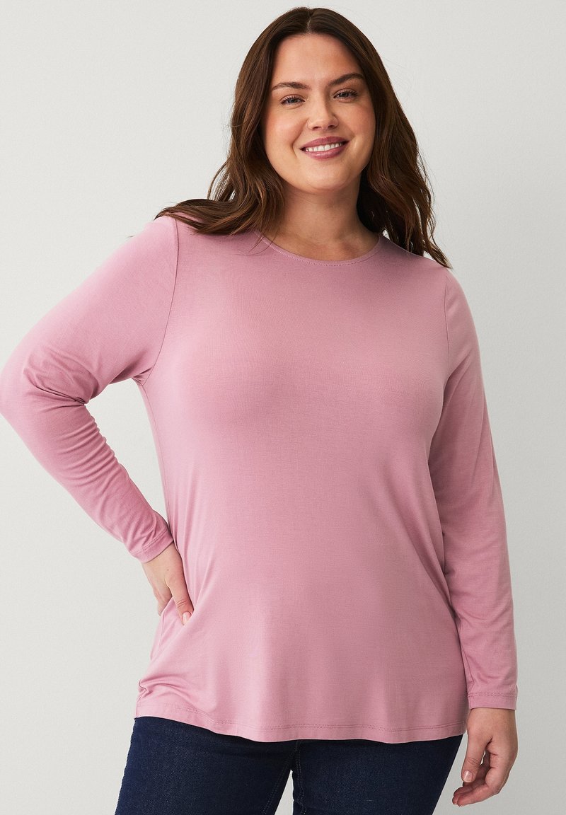 Long-sleeve pink top made of soft fabric, featuring a round neckline and a relaxed fit, paired with dark blue jeans.